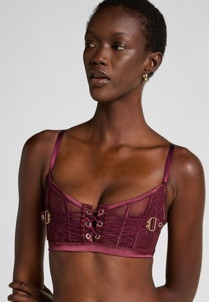 Bordeaux kant bralette met satijnen bandjes, voorzien van gouden hardware en een vlechtsluiting aan de voorkant, textuurdesign en doorschijnende panelen.