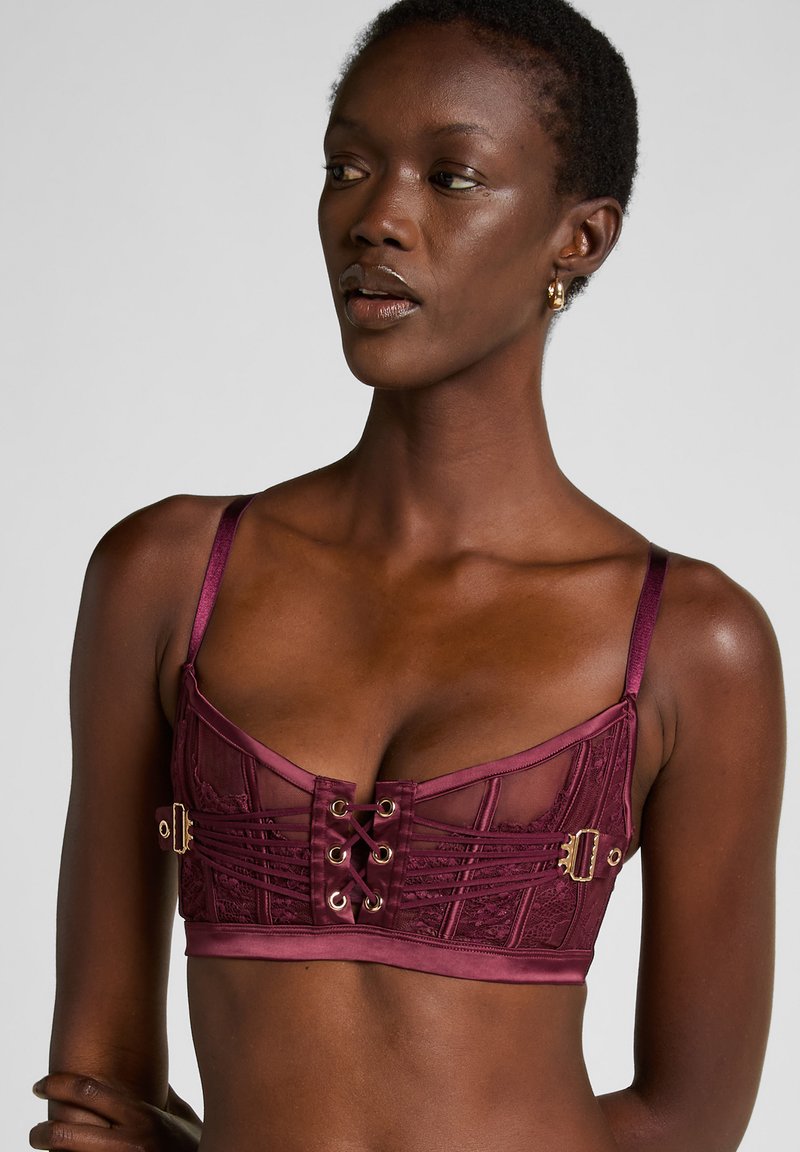 Bordeaux kant bralette met satijnen bandjes, voorzien van gouden hardware en een vlechtsluiting aan de voorkant, textuurdesign en doorschijnende panelen.