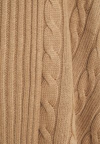 Stickad tröja i en varm beige färg med en blandning av ribb- och flätstickade mönster som framhäver textur och djup.