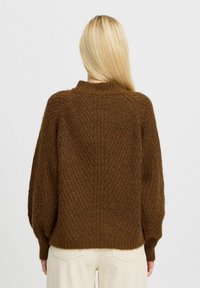 Pulover tricotat maro cu un model texturat, guler înalt și mâneci largi, asociat cu pantaloni din bumbac corduroy de culoare deschisă.
