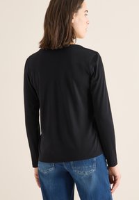 Schwarzes Langarmshirt mit Rundhalsausschnitt, aus weichem Stoff, figurbetontem Design und glatter Textur. Kombiniert mit blauen Denim-Jeans.