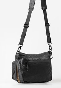 Borsa a tracolla nera in nylon con cinturini regolabili, scomparti con cerniera, texture liscia e design minimalista. Presenta dettagli in metallo.