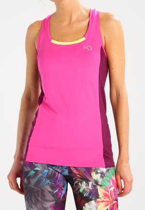 Kvinde iført en skrigpink ærmeløs træningstop og farverige leggings med blomsterprint, stående mod en ensartet lys baggrund.