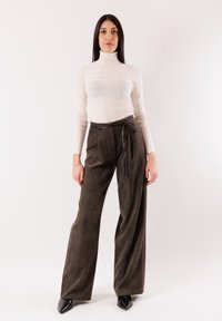 Top crema a collo alto con trama a coste, abbinato a pantaloni a gamba larga marrone scuro a vita alta con coulisse e sottile lucentezza.