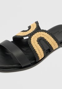 Sorte lærsklisandal med en vevd halmstropp som har et svart og gult sikk-sakk-mønster, designet for komfort og stil.