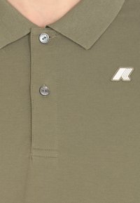 Polo verde oliva con un tessuto testurizzato, due bottoni e un piccolo logo bianco sul lato sinistro vicino al colletto.