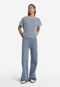 Ljusblå blus med kort ärm i ett flödande tyg, i kombination med ljusblå vida byxor, accentuerat med ett smalt vitt bälte och skor.