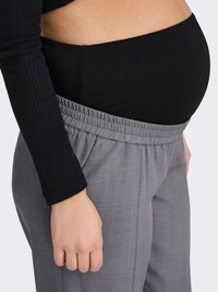 Haut de maternité noir associé à un pantalon gris extensible avec une taille élastique et des poches latérales, vu de profil.