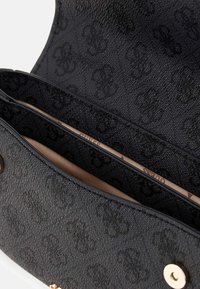 Interno di una borsa a tracolla in pelle nera texture, con due scomparti rivestiti in tessuto liscio e hardware dorato.