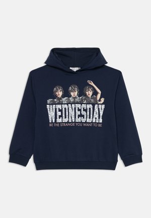 Hoodie bleu marine avec trois femmes illustrées au-dessus du grand texte blanc "WEDNESDAY" et du texte plus petit "SOYEZ L'ÉTRANGE QUE VOUS VOULLEZ ÊTRE."