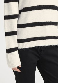 Black and white striped sweater with a soft texture, featuring wide black stripes on a cream background and ribbed cuffs.