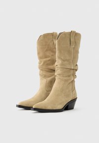 Bottes de cowboy en daim beige avec un design décontracté, bout pointu et un petit talon noir empilé. Avec des languettes en haut pour un enfilage facile.