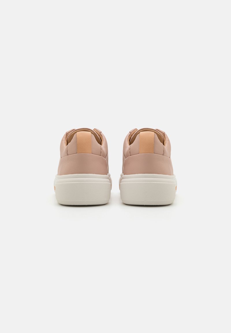 Zapatillas sintéticas rosas con una textura suave, acentos en un tono claro de marrón en el talón y una suela de goma blanca. Vista trasera mostrada.