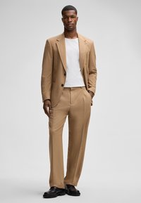 Beige Wollsakko mit einem Zweiknopf-Blazer und geraden Hosen. Kombiniert mit einem weißen Rundhalsausschnittshirt und schwarzen Schuhen. Glatte Textur.