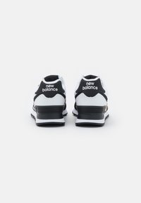Baskets New Balance en noir et blanc avec une semelle texturée, dotées d'un col rembourré et d'un logo blanc sur le talon.