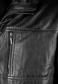 Close-up van een zwarte leren jas met een gestructureerd oppervlak, verticale ritstas, en kraag met zichtbare stiksels en metalen ritstanden.