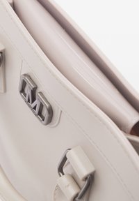 Witte leren handtas met zilverkleurige hardware, voorzien van een opvallend logo en een gladde textuur. Inclusief straps en een gestructureerde vorm.