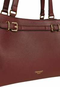 Borsa a tracolla in pelle bordeaux con finiture dorate, due cinghie per la spalla e una finitura testurizzata. Include un dettaglio del logo in oro sul davanti.