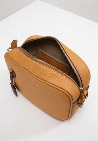 Żółta skórzana torba na ramię z zamkiem błyskawicznym. Wewnątrz wyściełana materiałem i posiada skórzany uchwyt na karty. Ozdobiona złotymi elementami i dekoracyjną metką.