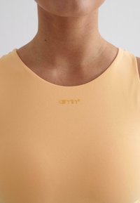 Peachkleurige tanktop met een gladde textuur, voorzien van een ronde halslijn en een subtiele logo in bijpassende kleur op het borstgebied.