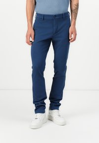 Pantalon bleu marine ajusté, en tissu extensible, avec une fermeture à bouton et des poches latérales, assorti à des baskets blanches.