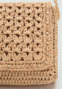 Woven-Handtasche aus natürlichen Fasern in einem hellbeigen Farbton, mit einem strukturierten floralen Muster, goldfarbener Hardware und einem Kettenriemen.