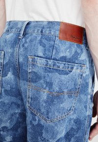 Svetlomodré džíny z denimovej tkaniny s textúrovaným umývaním, vybavené dvoma zadnými vreckami a hnedou koženou etiketou s vyrazeným nápisom "Pepe Jeans".