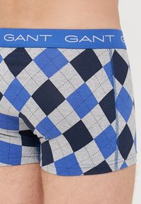 Boxeri cu un model gri și albastru, decorati cu un design în romb, având un brâu albastru cu logo-ul "GANT" și cusături albastre contrastante.
