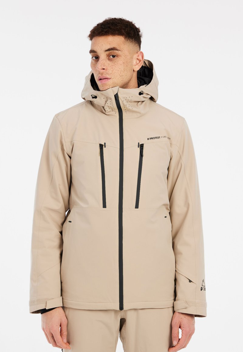 Beige waterdichte jas met capuchon, voorzien van zwarte ritsen, twee voorzakken en ventilatiegaten bij de kraag. Gladde textuur.