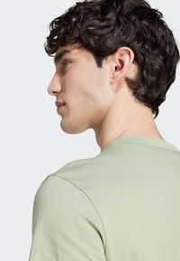 Camiseta de cuello redondo verde claro, hecha de una tela suave, con mangas cortas y un corte relajado, vista de lado con líneas de hombros definidas.