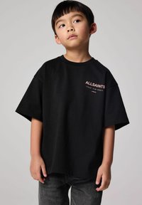 Juoda trumpa rankovėmis marškiniai, laisvo kirpimo, su rožiniu logotipo tekstu "ALLSAINTS" ant krūtinės. Dėvimi su tamsiai pilkomis džinsinėmis kelnėmis.