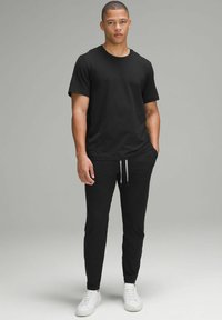 Sort bomulds T-shirt og sorte joggers med snøre. Modellen bærer hvide sneakers. Enkel, afslappet design med en tætsiddende silhuet.