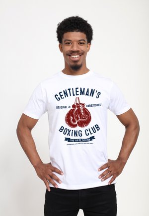T-shirt en coton blanc avec un imprimé graphique de gants de boxe en texte rouge et bleu, étiqueté "Gentleman's Boxing Club", col rond.