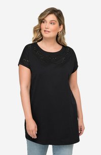 Camiseta negra de manga corta, cuello redondo y patrones decorativos recortados a lo largo del escote y las mangas. Corte casual, textura suave.