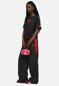T-shirt noir court avec le texte rouge "Formula 1 Racing", associé à un pantalon noir avec des rayures latérales rouges et un petit sac à main Puma rouge.