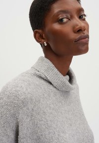 Grauer Rollkragenpullover aus strukturiertem Strickmaterial mit lockerer Passform. Verfügt über einen hohen Kragen und subtile Farbvariationen.