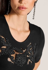 Schwarzes Top mit einem Rundhalsausschnitt, das mit ausgeschnittenen Designs und Strassverzierungen für Textur versehen ist. Glattes Material und taillierte Form.