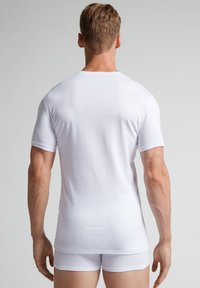 Weißes kurzärmliges T-Shirt aus glattem Stoff, taillierte Passform, mit rundem Halsausschnitt und einfacher Saum, von hinten gezeigt.