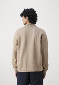 Felpa color khaki con scollatura rotonda, maniche lunghe e vestibilità rilassata. Tessuto liscio con cuciture minime e un piccolo dettaglio del logo all'orlo.