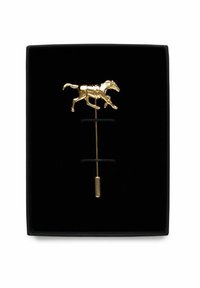 Gul hästformad klämsmärke med detaljerad design, med en lång rak nål och en cylindrisk bas, visad mot en svart sammetbakgrund.