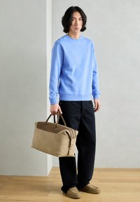 Felpa azzurra con polsini a coste, pantaloni neri a gamba larga e borsa in pelle marrone con dettagli beige. Calzature casual completano l'outfit.