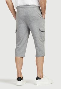 Graue Baumwoll-Cargo-Shorts mit elastischem Bund, seitlichen Taschen und knielangem Schnitt, präsentiert mit einem weißen Sneaker.