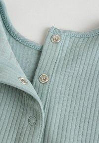 Tissu côtelé bleu clair avec des boutons-pression en argent au niveau du col. Gros plan mettant en valeur la texture et le détail des boutons.