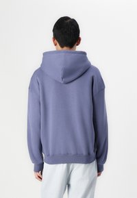 Lilla oversized hættetrøje med snøre i hætten, ribbede manchetter og en blød tekstur. Modellen har lyse denim bukser på.