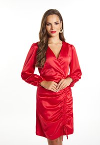 Rochie din satin roșu cu mâneci lungi și puff, decolteu în V și detalii pliate pe lateral. Prezintă textură plisată și sfoară ajustabilă la tiv.