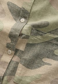 Camo-gepatteerde shirt met tinten groen en beige. Gemaakt van textuurstof met een knoopsluiting en een borstzakdetail.