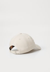 Cappellino da baseball beige con visiera curva, realizzato in tessuto testurizzato. Presenta una chiusura snapback e una patch decorativa all'interno.