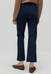 Marineblauwe flared broek van textuurstof, met een hoge taille en twee achterzakken, gecombineerd met bruine suède ballerina's.