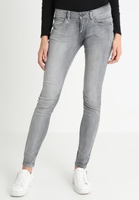 Jeans ajustados grises de mezclilla con un ligero estiramiento, que presentan un diseño clásico de cinco bolsillos y una cremallera, combinados con zapatillas blancas.