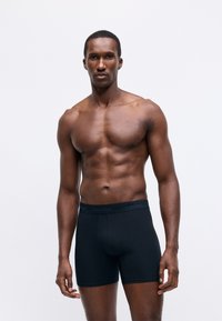 Fekete pamut boxer alsónemű, testhezálló kialakítással, puha derékrésszel, amelyen "Calvin Klein" márkázás található. Sima textúra, combközép hosszúság.